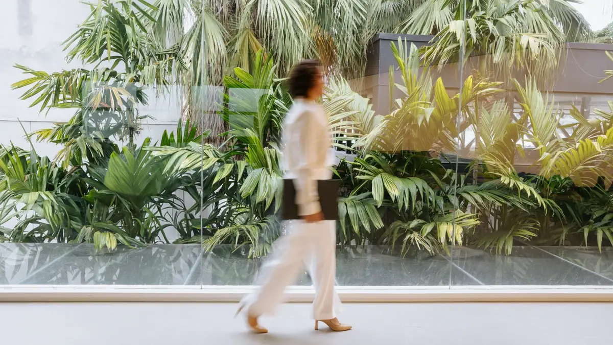 Débora Parreira caminhando apressada diante de um jardim, com o movimento borrado pela velocidade